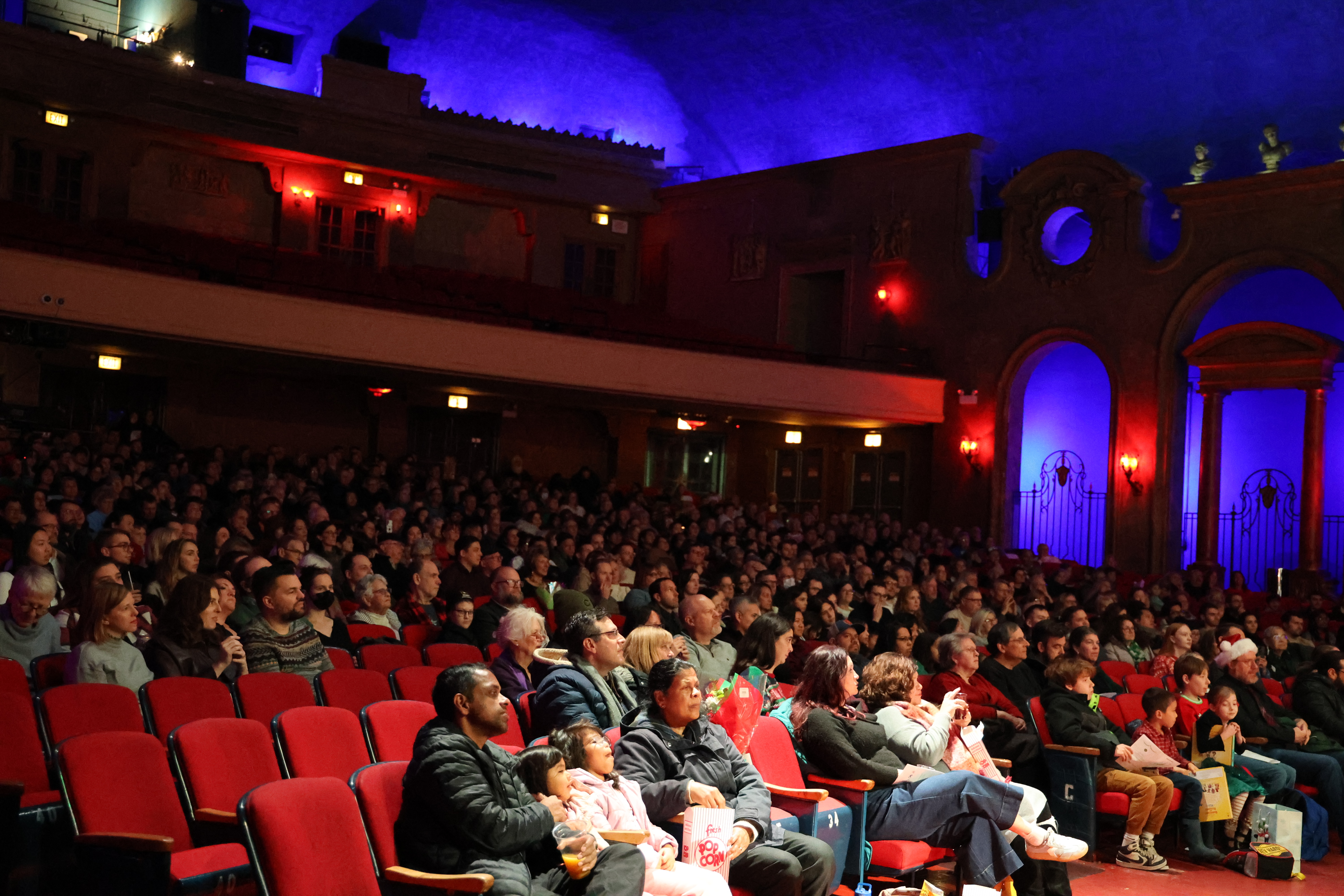 Audience fills theater seats with red lighting.